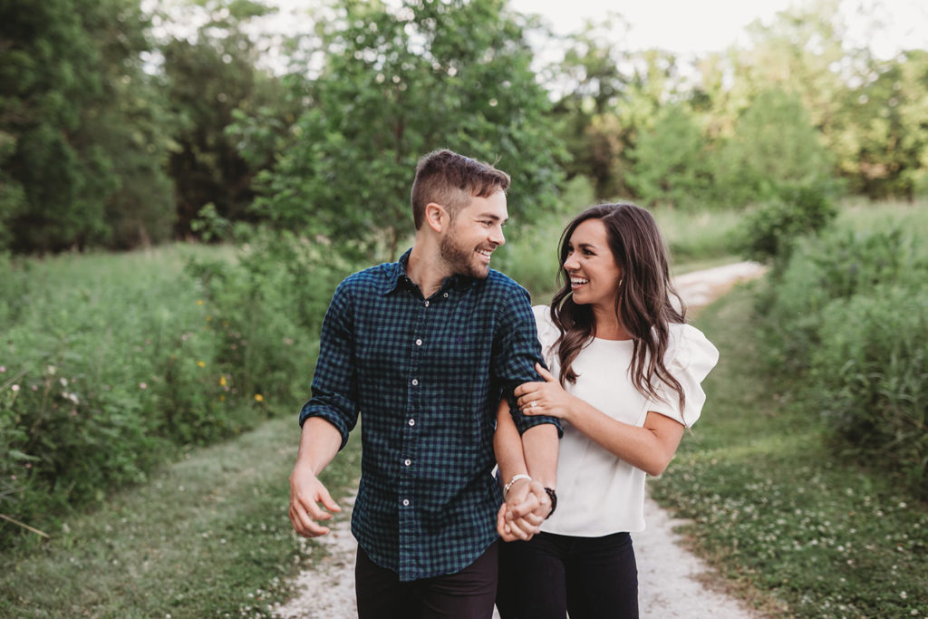 man and woman hold hands and walk down path during their Hamilton county engagement portraits