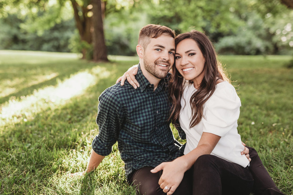man and woman sit on grass at sunset during their hamilton county engagement portraits