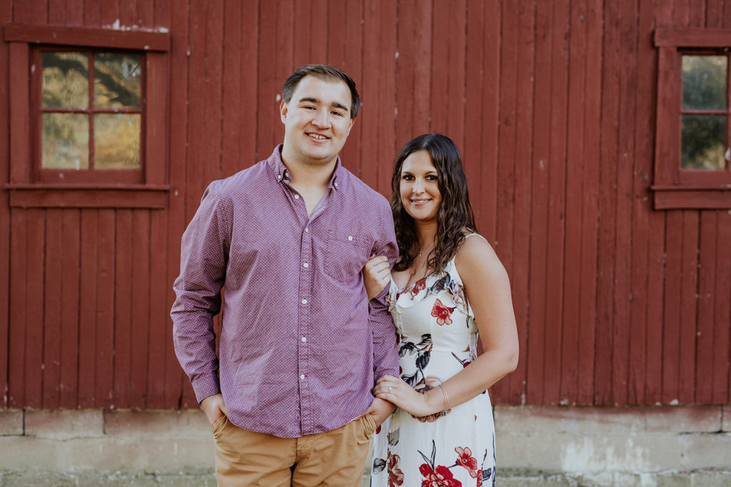 man and woman stand in front of red barn