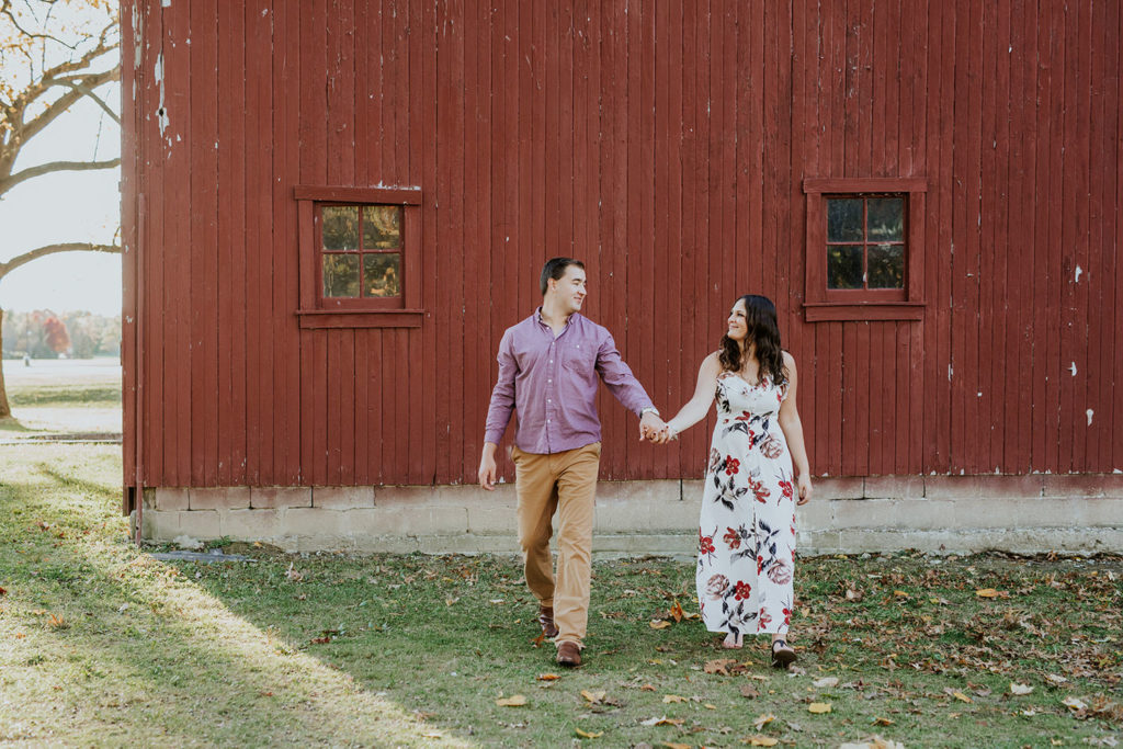 man and woman hold hands and walk away from red barn