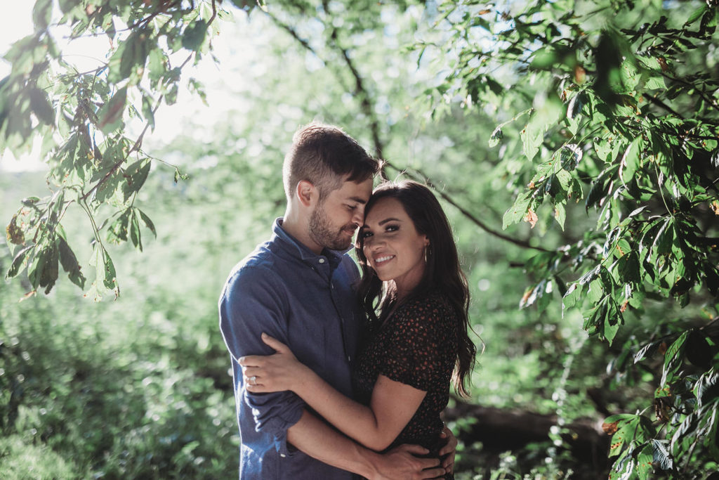 man and woman stand in the woods at their hamilton county engagement