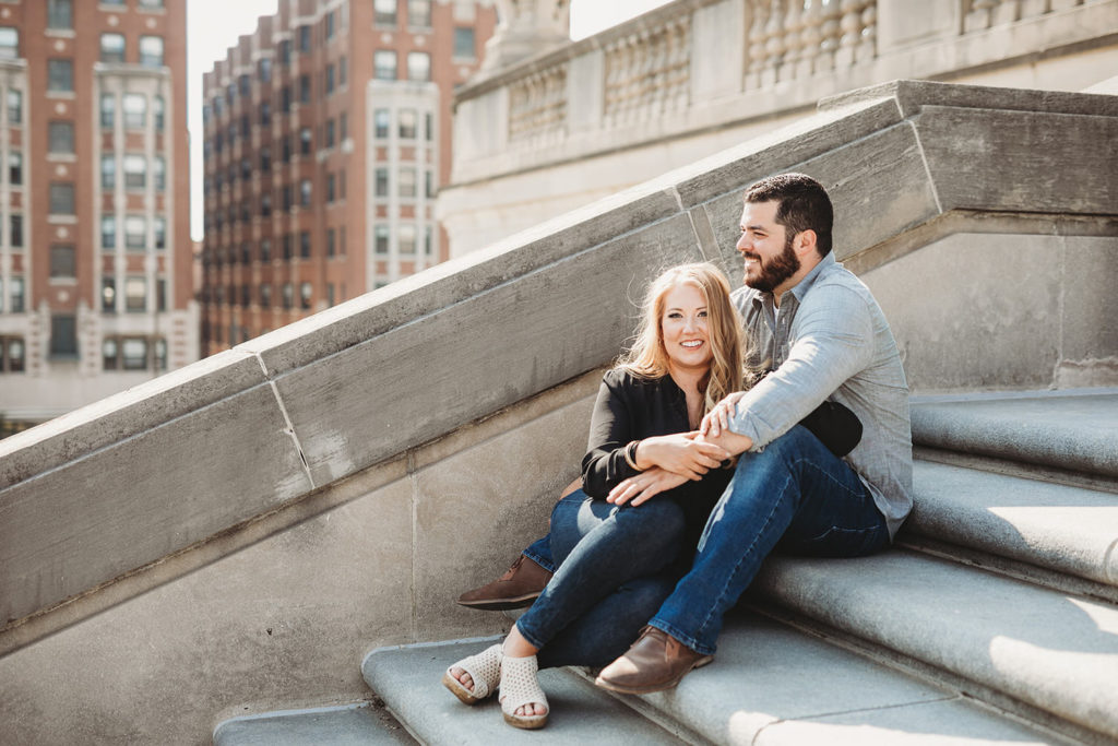 snuggly young couple with blonde and brown hair sit on steps of war memorial during their downtown indianapolis engagement photos