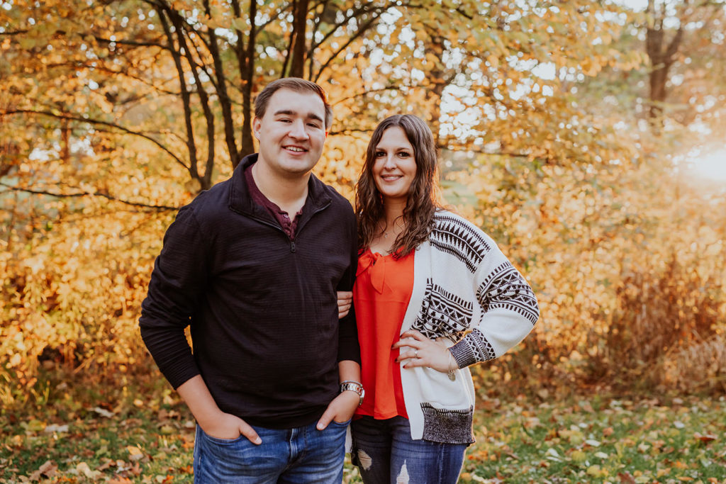 man and woman smiling in front of fall foliage