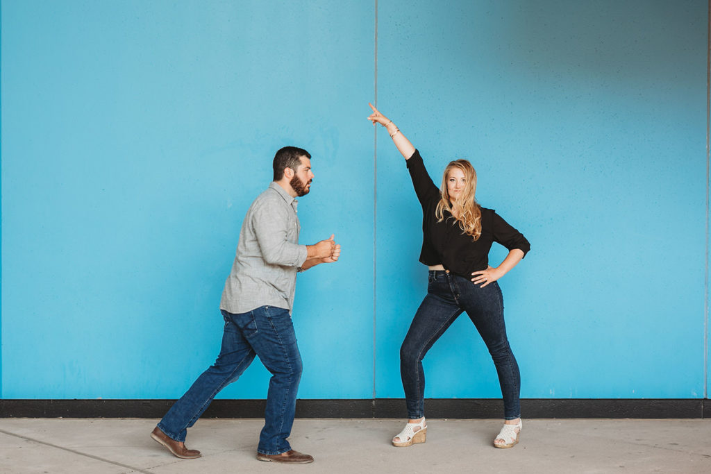 young couple dances in front of blue wall during their downtown indianapolis engagement photos