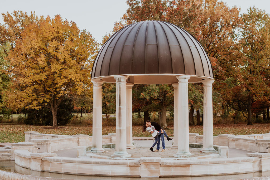 man dips and kisses woman under gazebo at their coxhall gardens engagement session