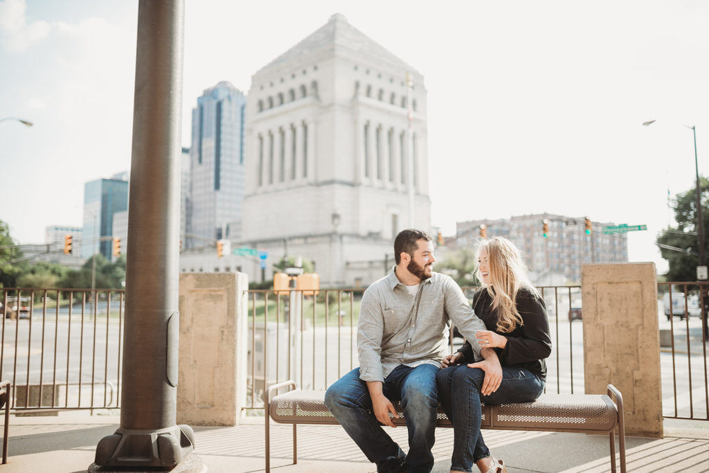 bearded man and blonde woman on bench look at each other while sitting on bench in front of indiana war memorial