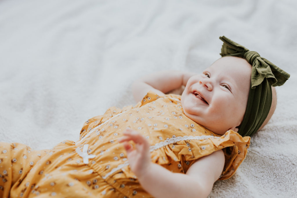baby girl with green headband laughing on white blanket in Indy family photos