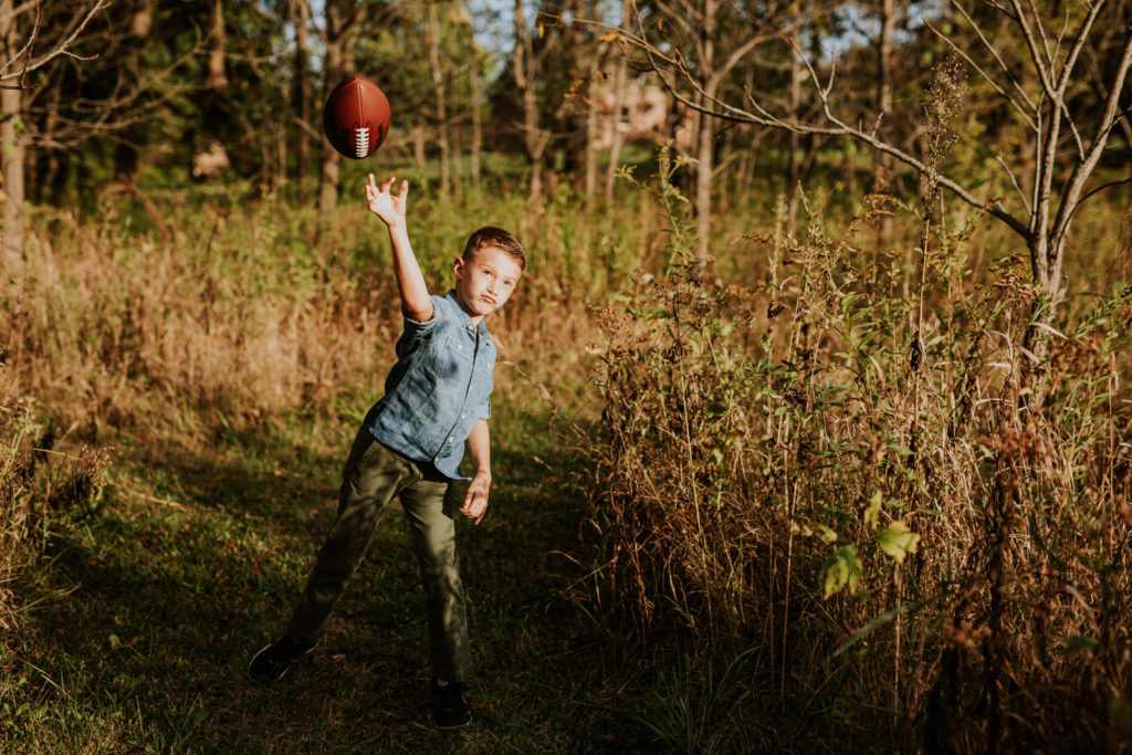 boy throws football in field in fall