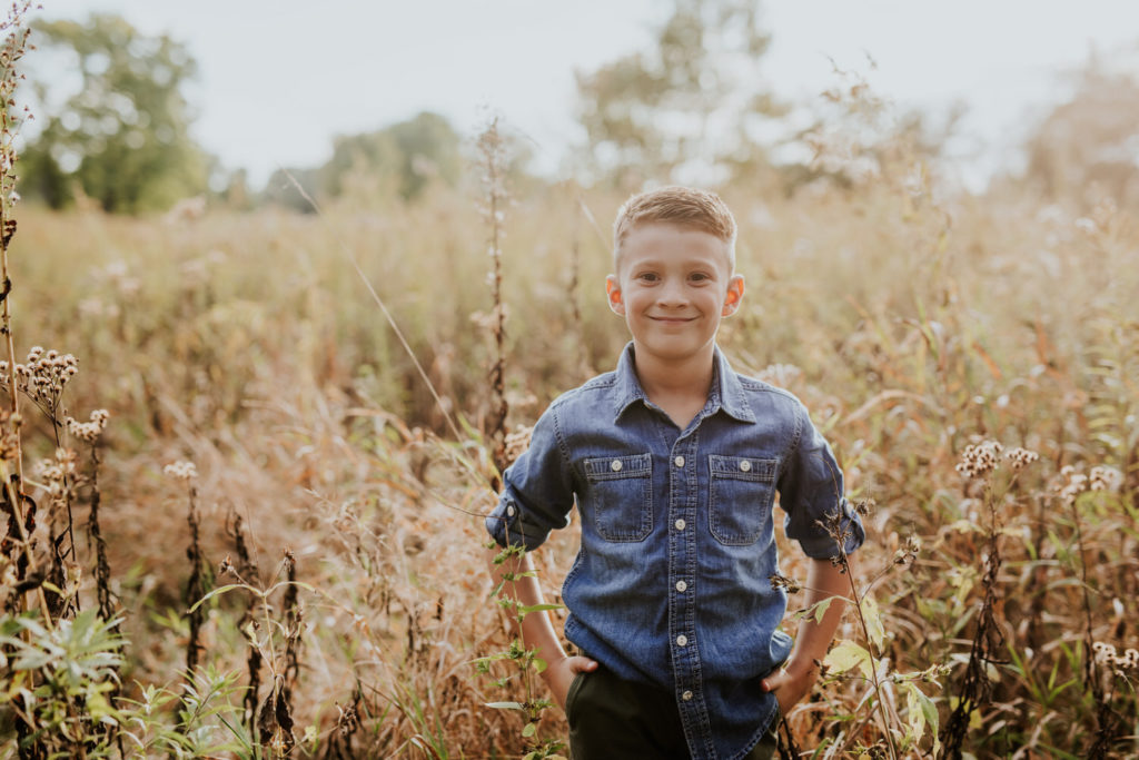 boy in denim shirt smiles with his hands in his pants pockets in Indy family photos