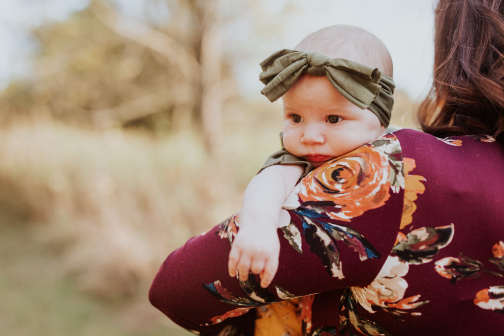 baby girl in green headband looks over her mother's shoulder in Indy family photos
