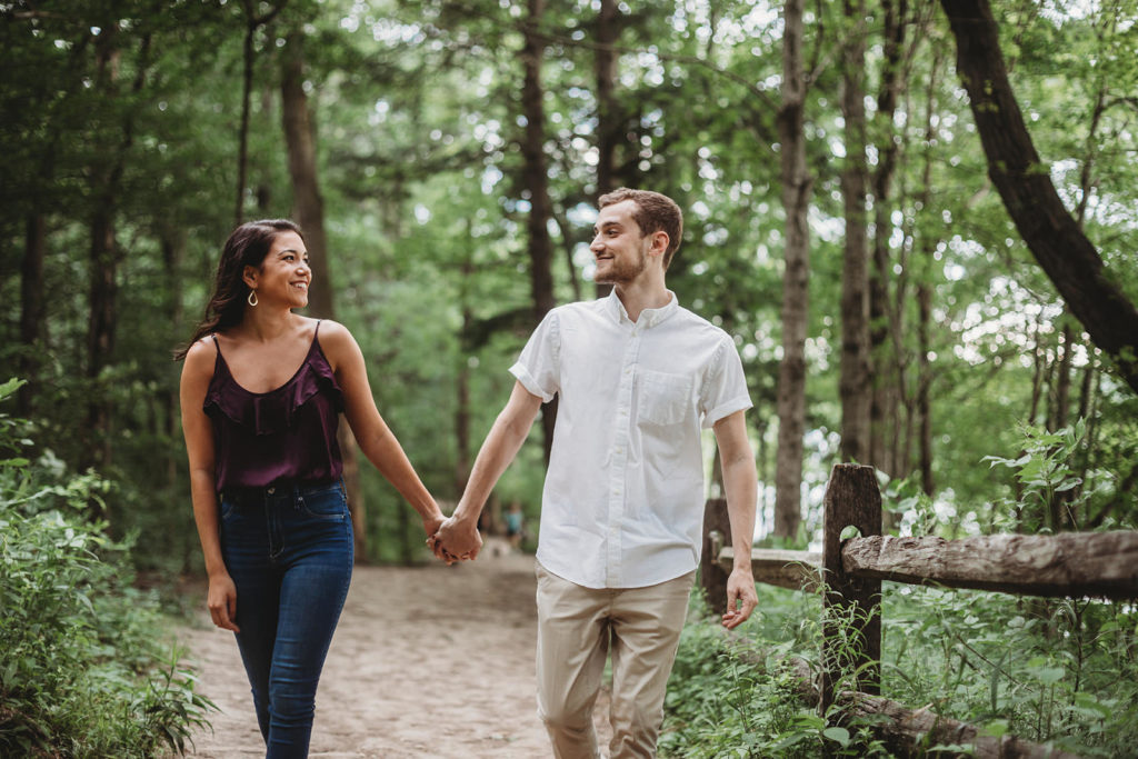 young couple walking hand-in-hand through the woods at an Indianapolis Park