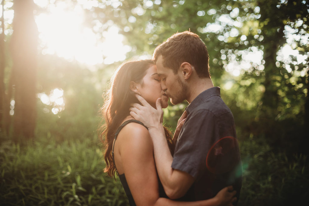 young couple kiss in front of sunset in the woods during their Eagle Creek Reservoir Engagement