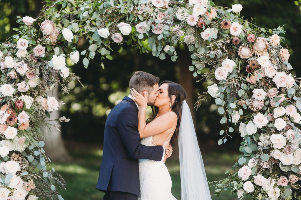 bride and groom kissing passionately in front of flower arch for their Carmel Backyard Wedding