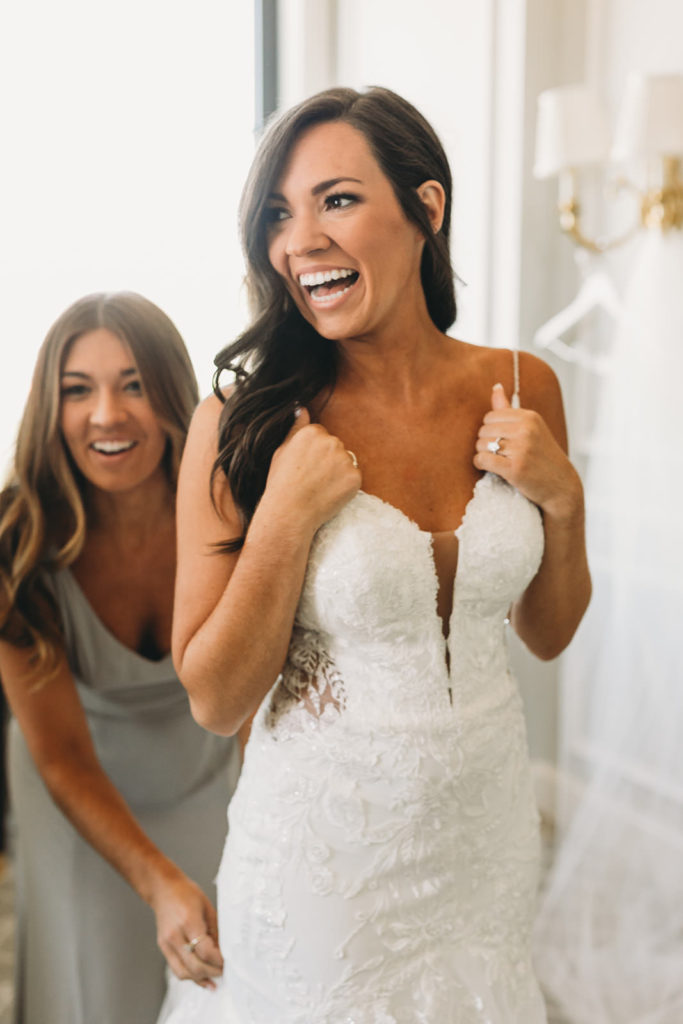 bride and sister laughing as bride gets into dress