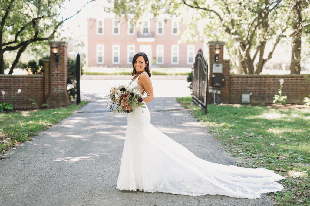 Bride stands in front of Coxhall Mansion holding flowers before her carmel backyard wedding
