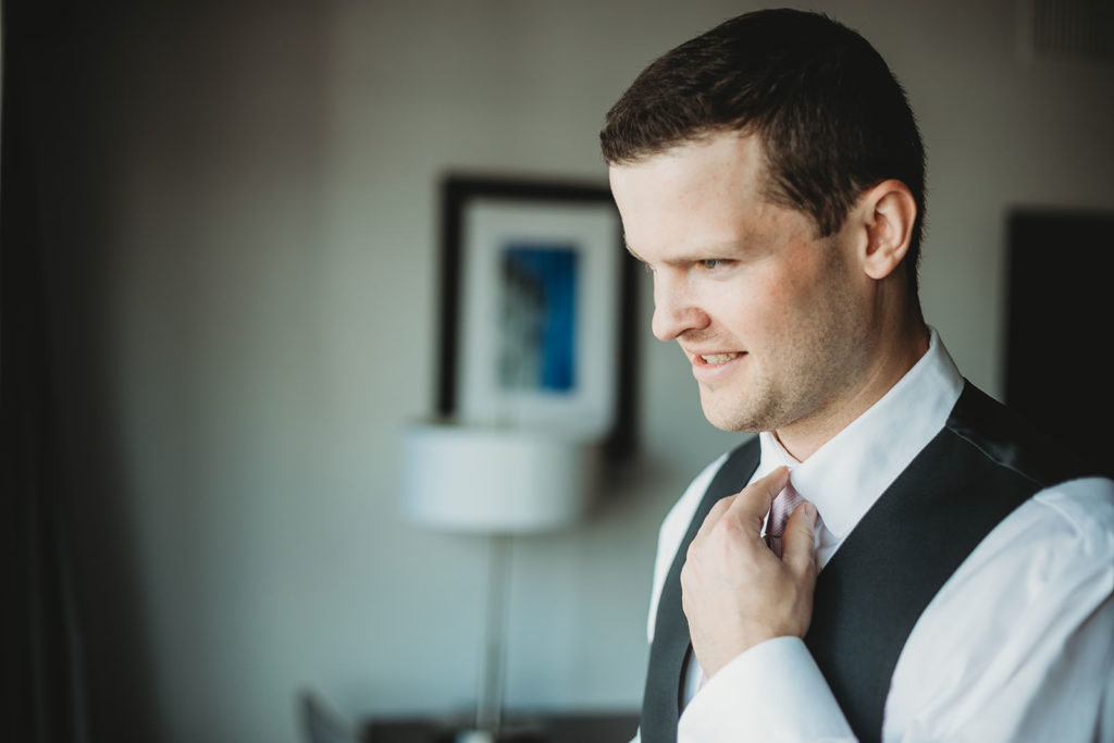 groom adjusts collar of shirt while getting ready for Indiana Roof Ballroom wedding