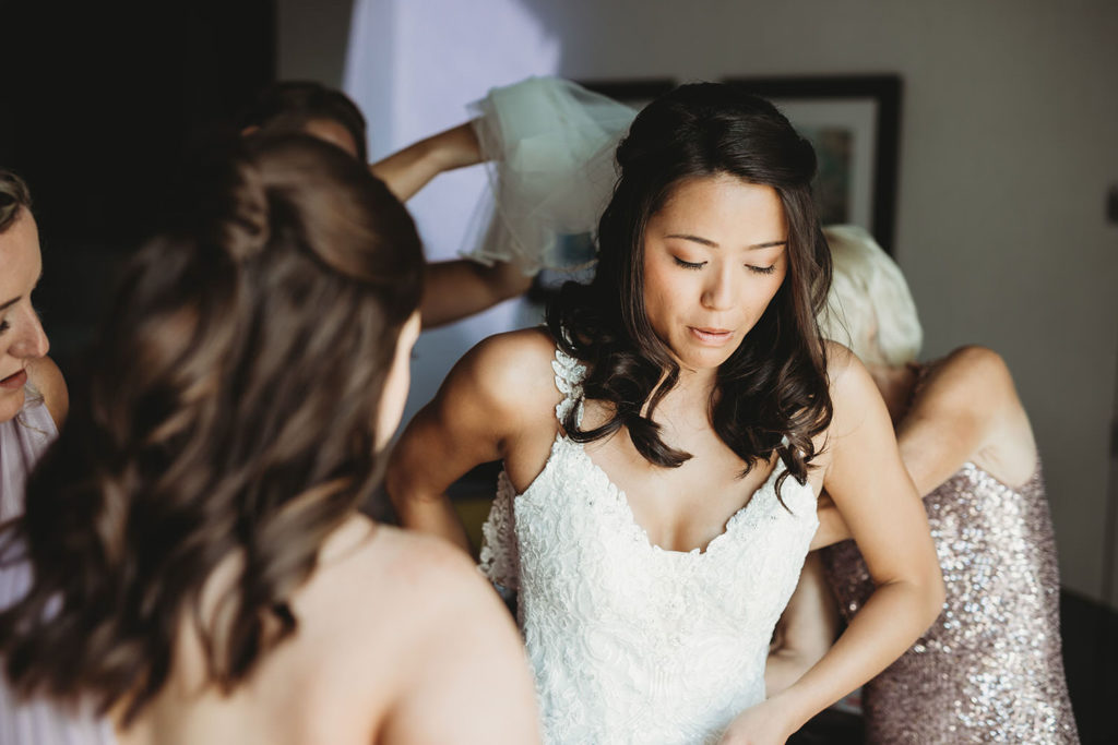 bride helped into wedding dress by several bridesmaids and mother for her Indiana Roof Ballroom wedding