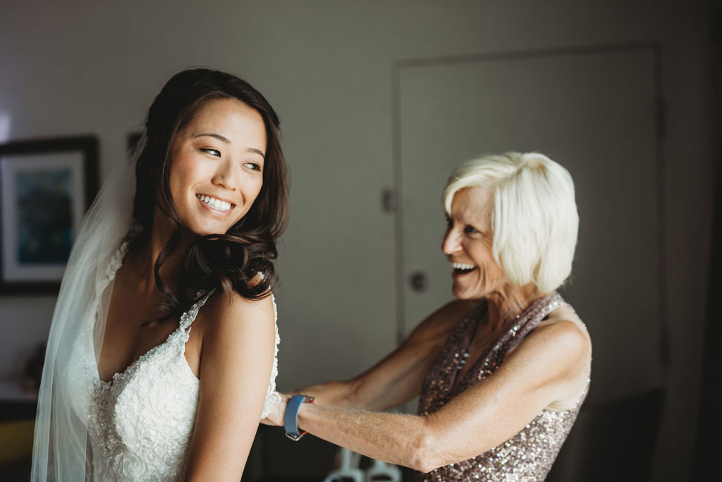 mother of bride smiles and zips up bride's dress before her Indiana Roof Ballroom wedding
