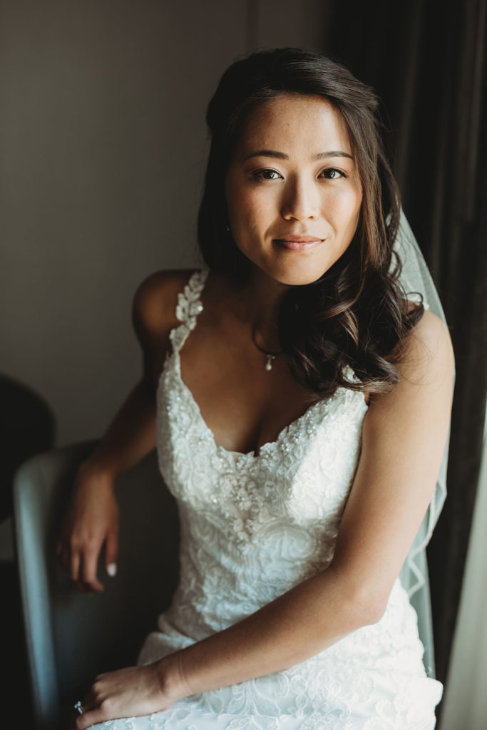 bride sits on chair and smiles in window light before her Indiana Roof Ballroom wedding