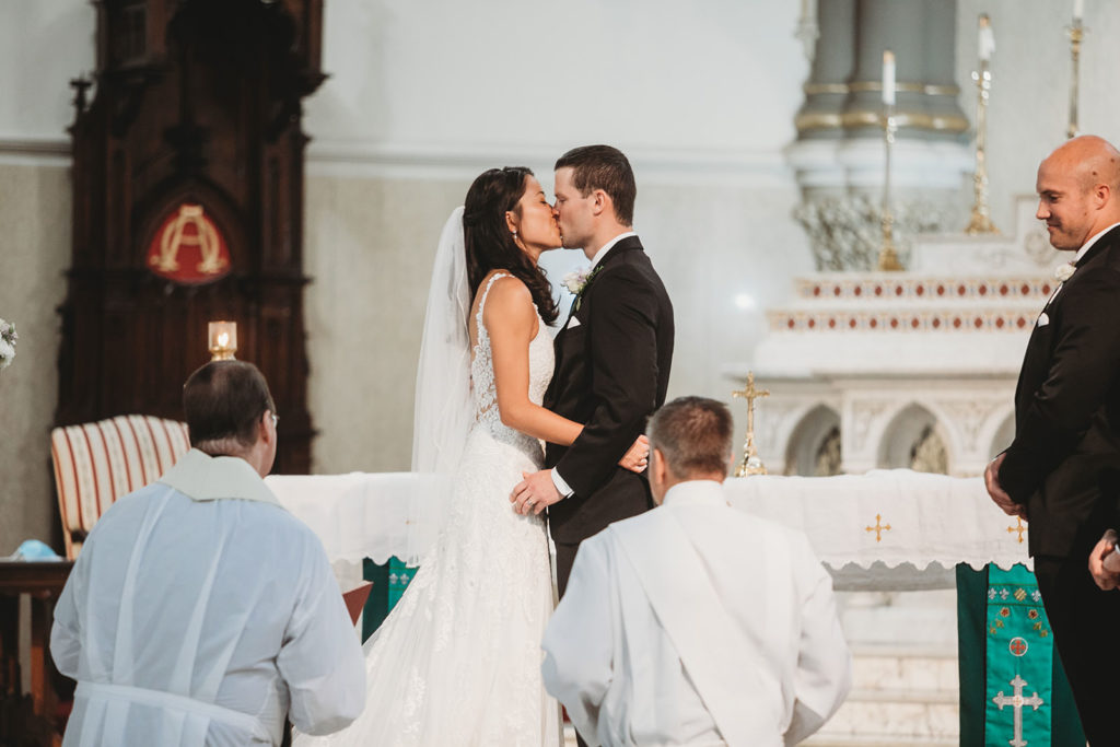 bride and groom share first kiss during wedding at St. John the Evangelist Catholic Church