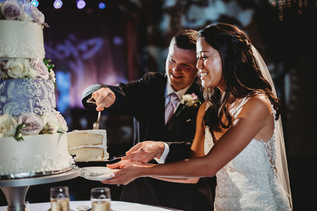 bride and groom remove large piece of cake from cake table to eat at their Indiana Roof Ballroom wedding