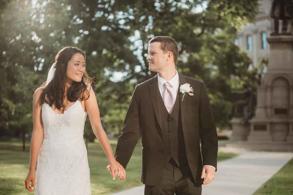 bride and groom hold hands and walk down sidewalk in front of indiana statehouse