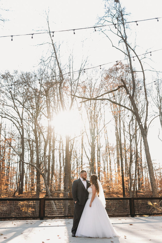 giant orb of setting sun penetrates sparse leaves on trees in fall while a bride and groom look into each other's eyes at a 3 Fat Labs wedding