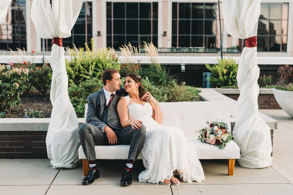 bride and groom cuddle on a white loveseat at a Regions Tower Wedding Celebration