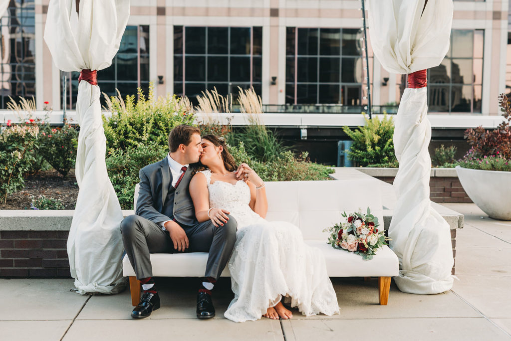 bride and groom sit on white feinting couch and kiss at a Regions Tower Wedding Celebration