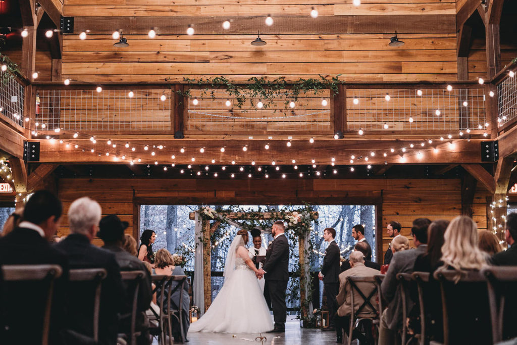wide shot of bride and groom at their 3 Fat Labs wedding with string lights and floral covered arch