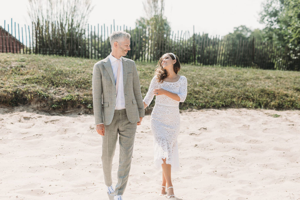 bride and groom hold hands and walk on beach at their traders point creamery wedding