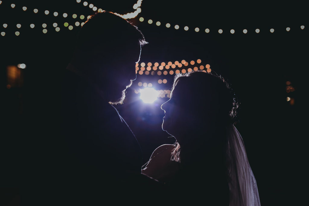 night shot of silhouetted bride and groom under string lights at their 3 Fat Labs wedding