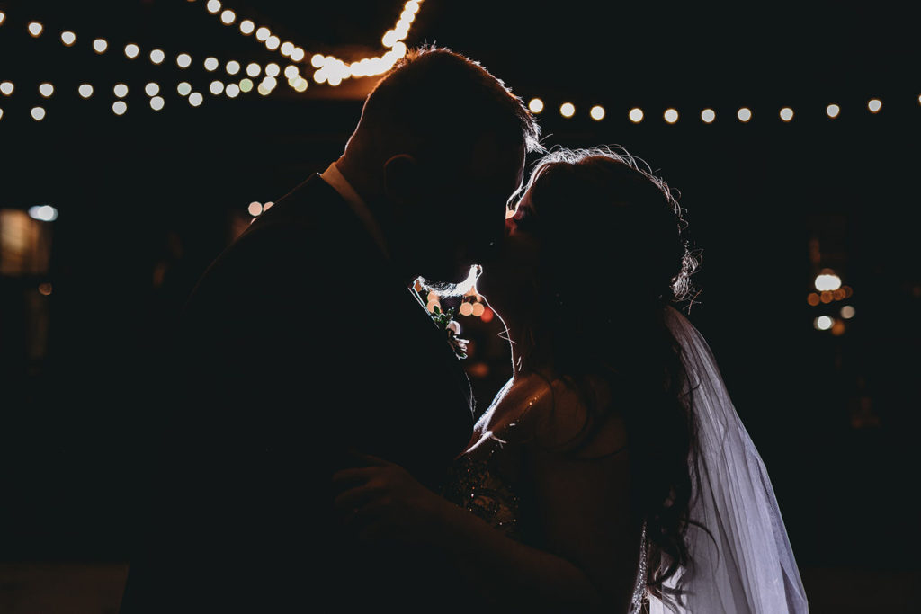 night shot of bride and groom kissing under string lights at their 3 Fat Labs wedding