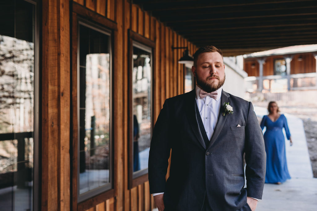 groom stands next to wood building while waiting to see his mom for the first time on his wedding day at a 3 Fat Labs wedding