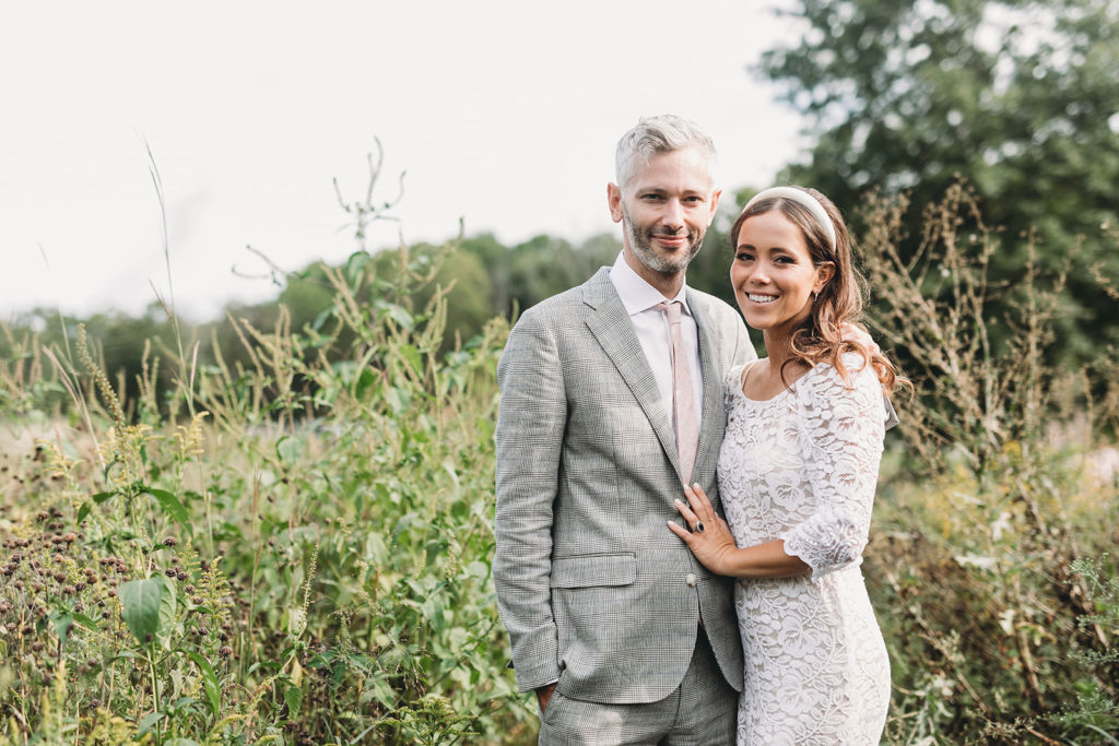 bride and groom stand in front of field of grass during their rustic zionsville wedding