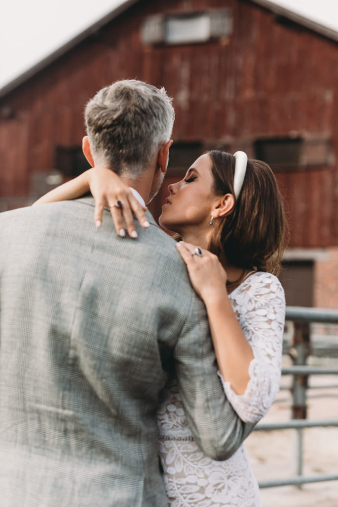 bride and groom kiss in front of red barn at a rustic wedding
