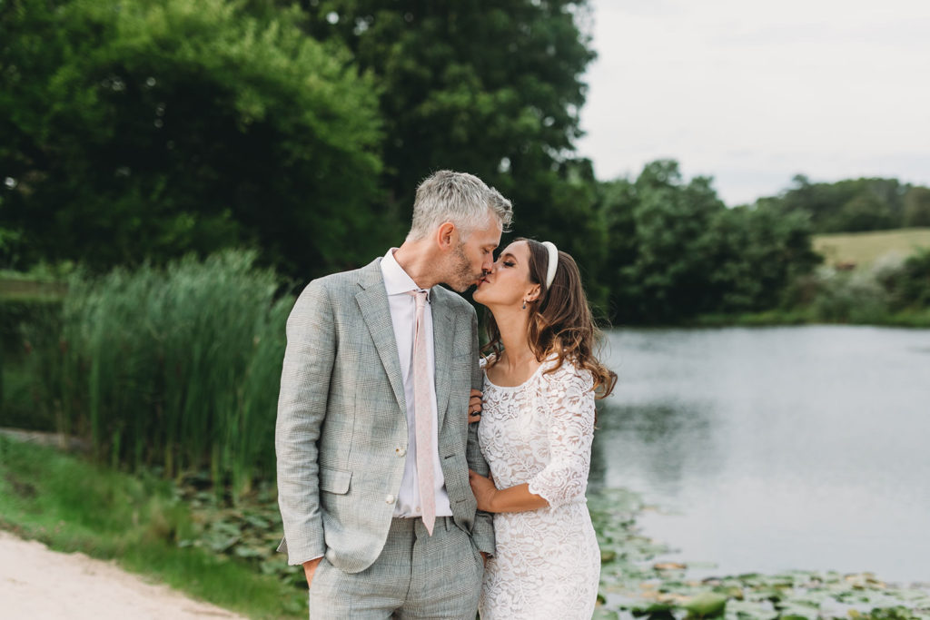 bride and groom kiss in front of pond and trees during their traders point creamery wedding