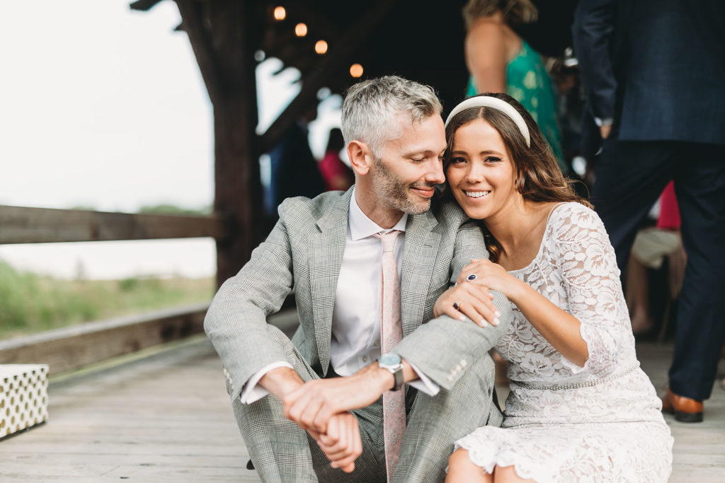 bride and groom sit down on beach porch and cuddle during their traders point creamery wedding