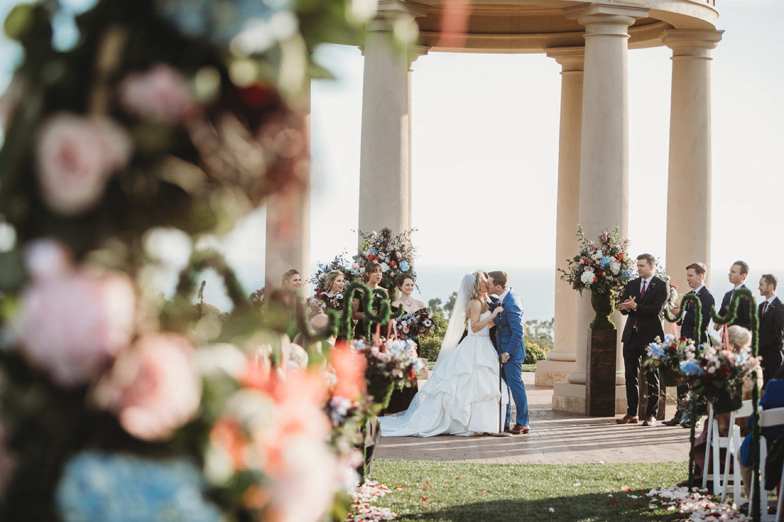 bride and groom kiss while framed by flowers in floral arch at a pelican hill wedding