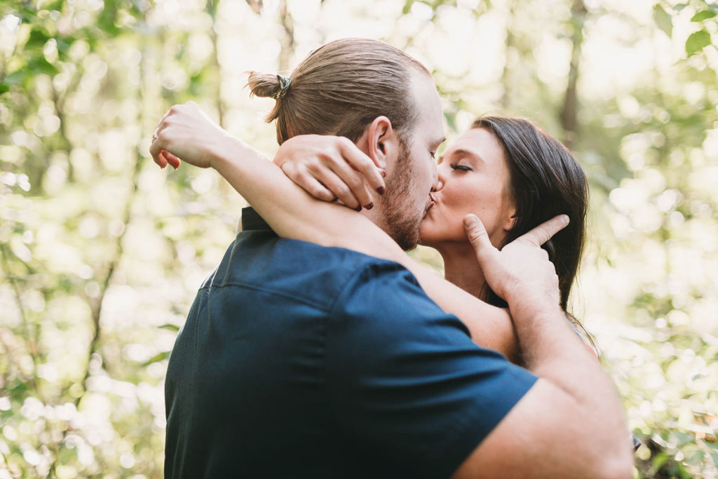 man with bun kisses woman in woods during their Arbuckle Acres engagement session