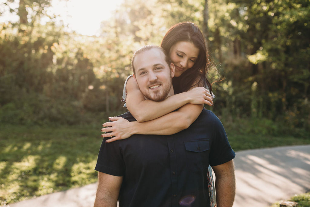 woman hugs man from behind around the neck during their Arbuckle Acres engagement session