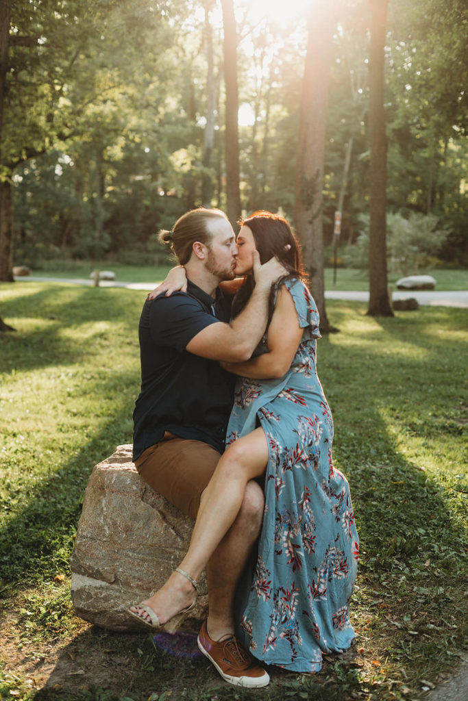 woman in green floral dress sits on man's lap and kisses him during their Arbuckle Acres engagement session
