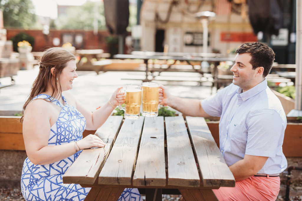 couple clink beers at a picnic table during their Rathskeller engagement session