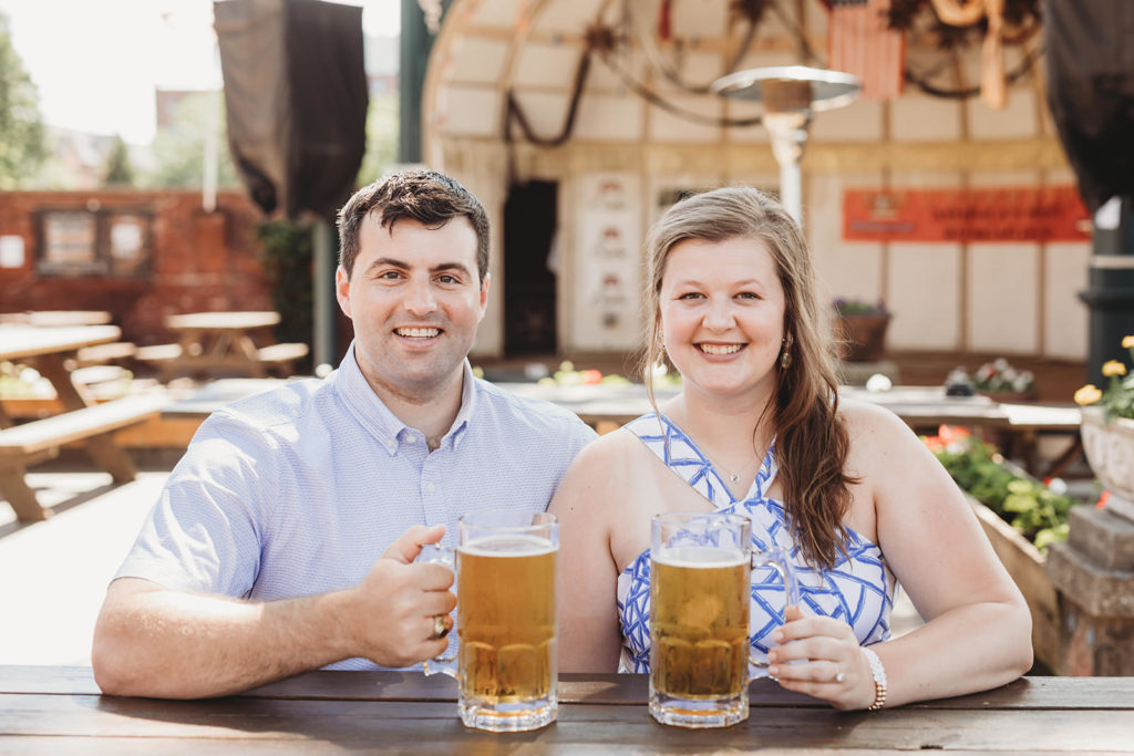 couple smile while holding giant mugs of beer during their Rathskeller engagement session