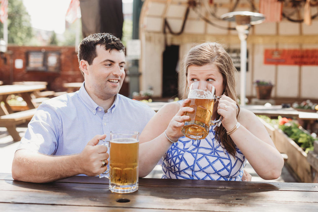woman drinks beer while man watches during their Rathskeller engagement session