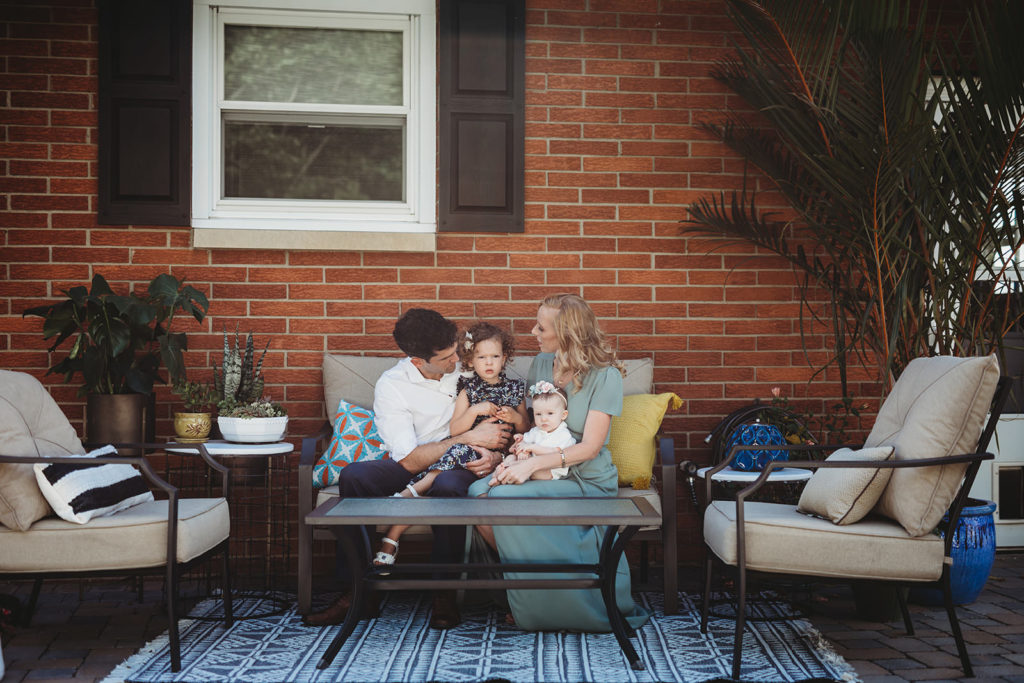 family sitting on patio furniture in front of brick house for this farmland family photography