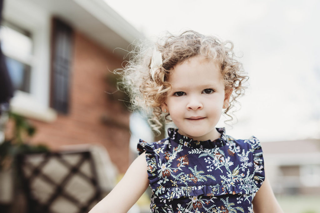 little girl with curly hair walks in front of house in this parker city family portrait