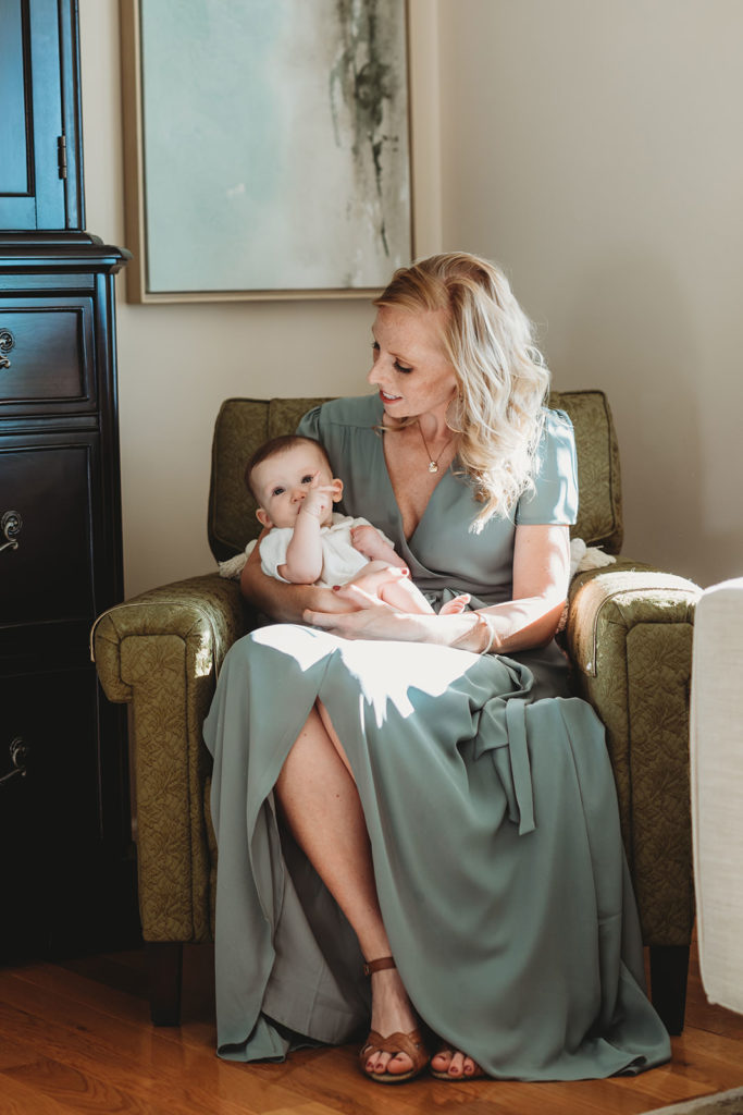 blonde mom holds baby girl in window light in this lifestyle family photography session in farmland