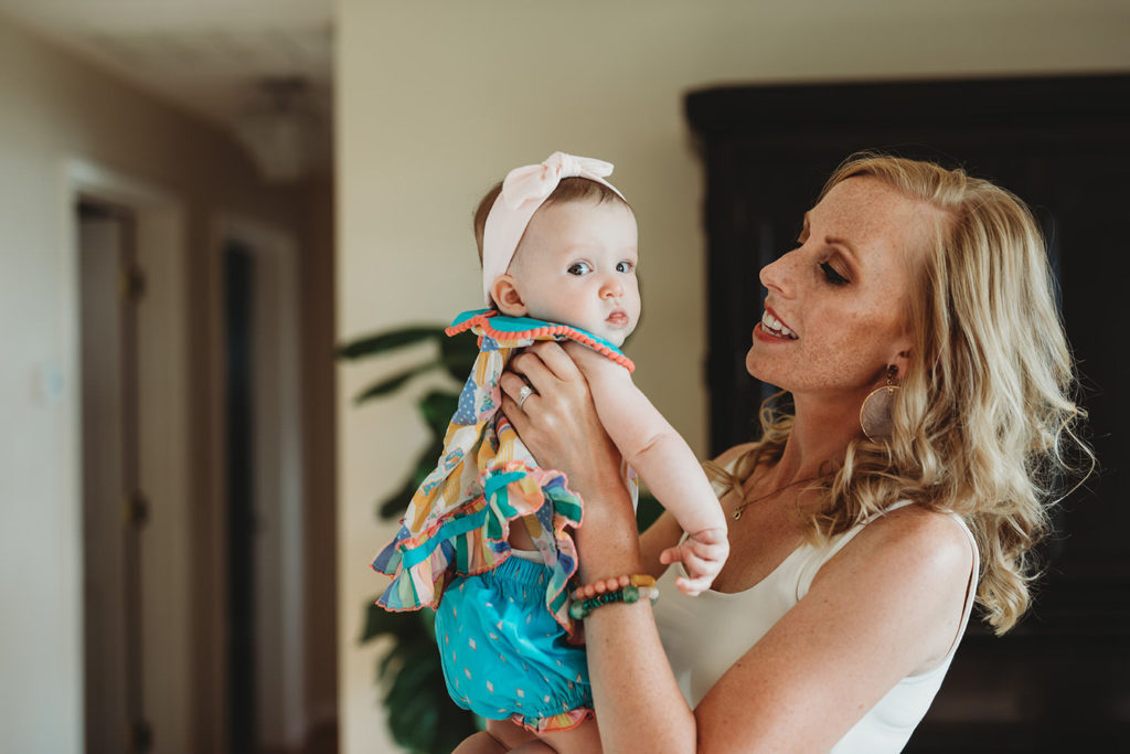 lifestyle photography blonde mom lifts baby daughter with pink headband up in this farmland family photography