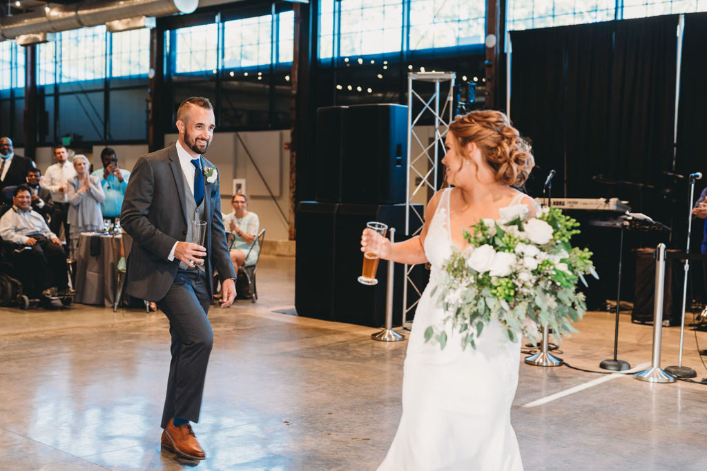 bride and groom enter reception while holding beers at a woolery mill wedding